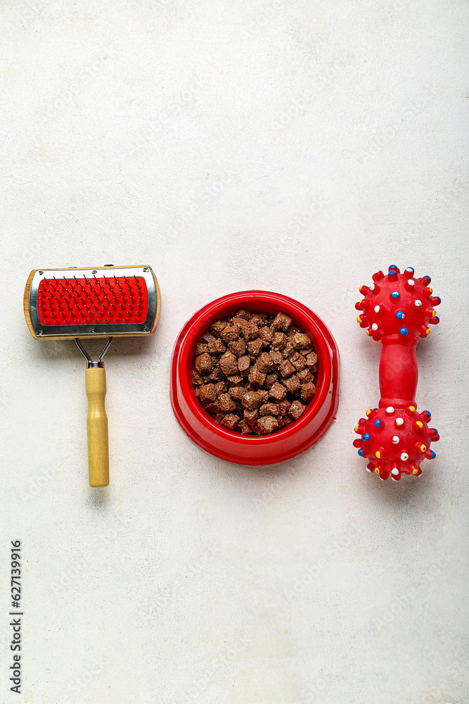 Bowl of wet pet food, toy and grooming brush on light background