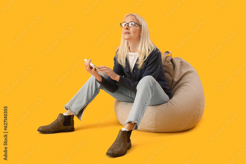 Mature female programmer working with computer keyboard in beanbag on yellow background