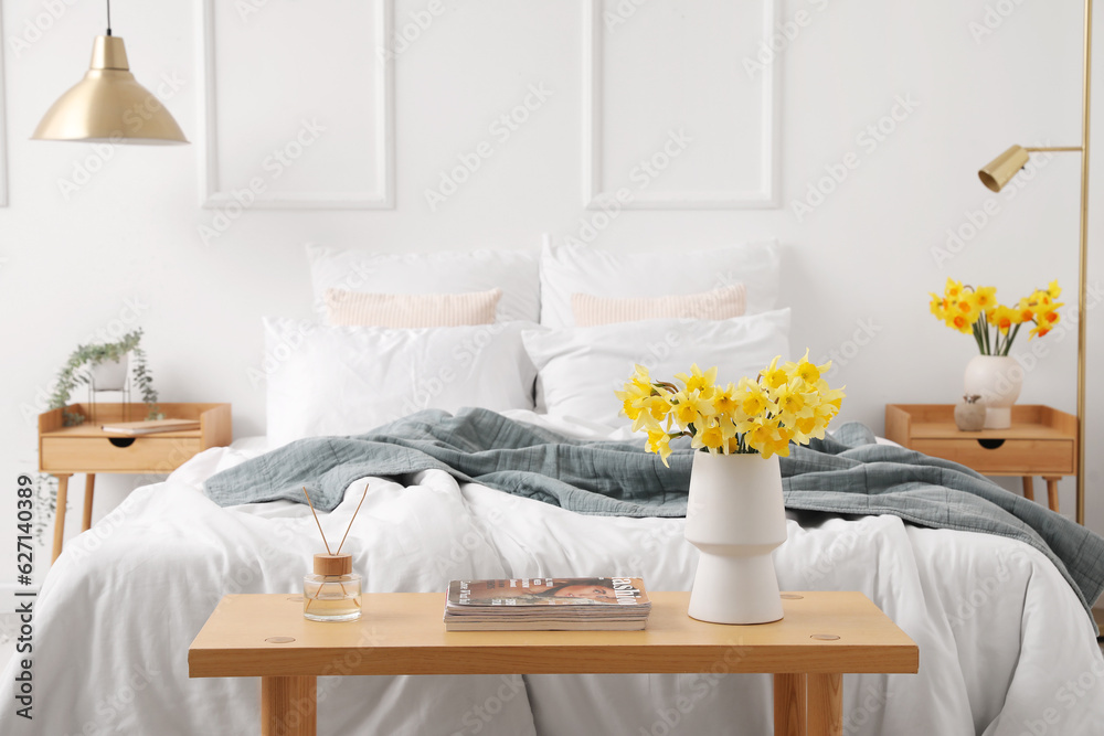 Interior of light bedroom with cozy bed and narcissus flowers on bedside table