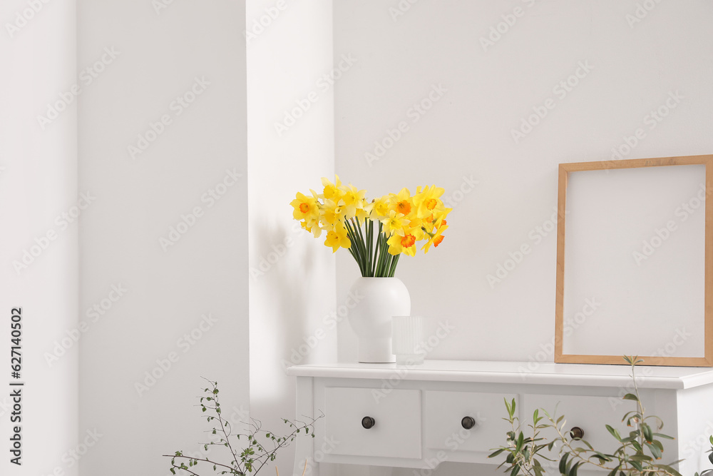 Vase with blooming narcissus flowers on dressing table in living room