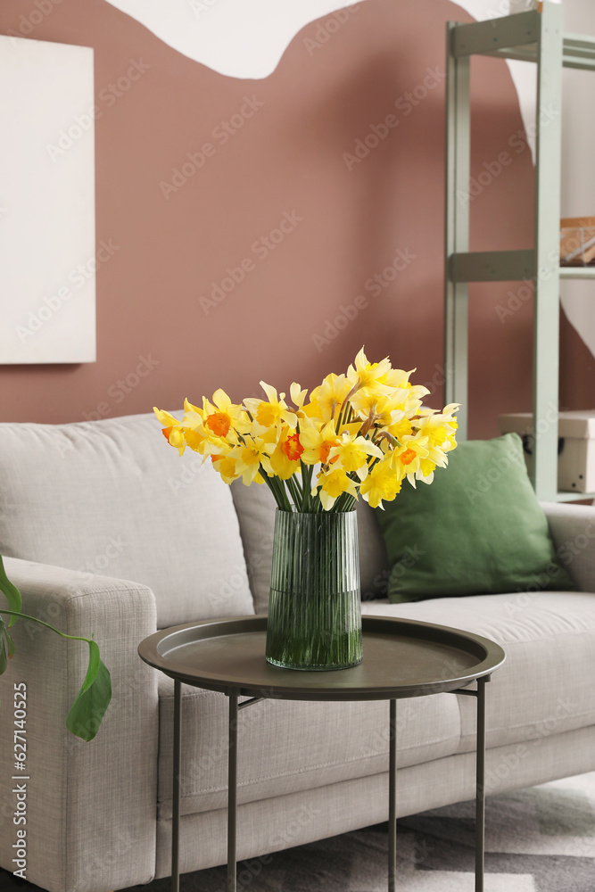 Vase with blooming narcissus flowers on coffee table in interior of living room