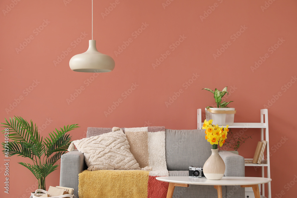 Grey sofa with cushions and blooming narcissus flowers on coffee table in interior of stylish living