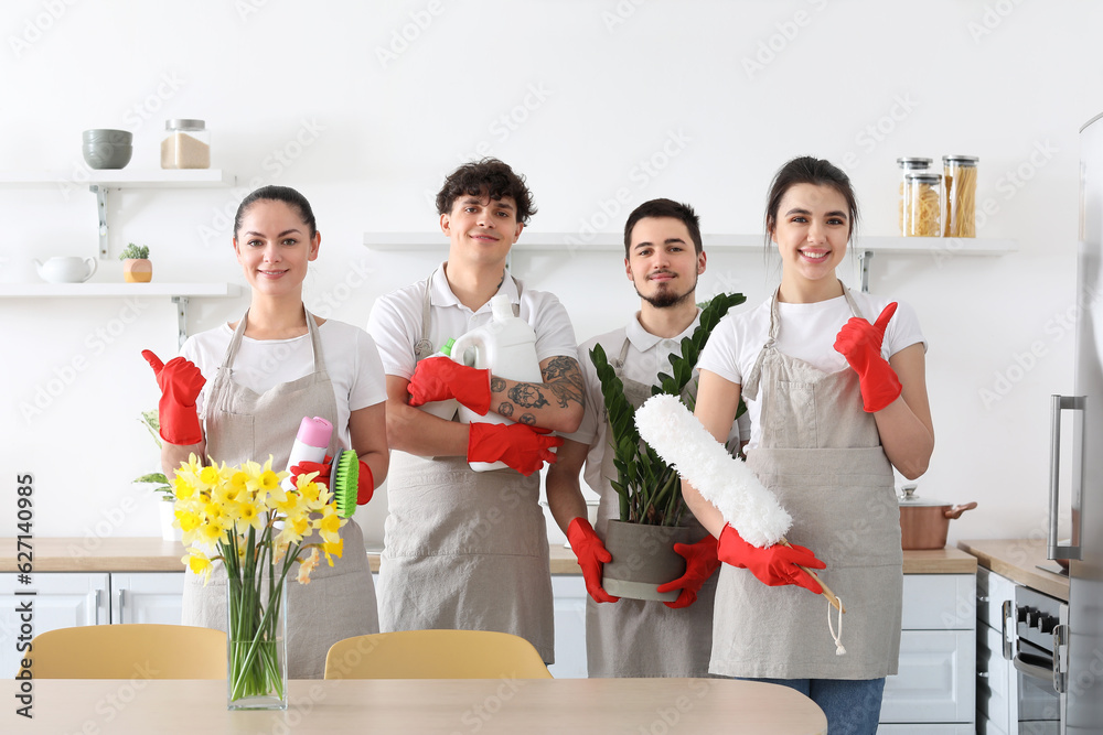 Young janitors with cleaning supplies and houseplant in kitchen