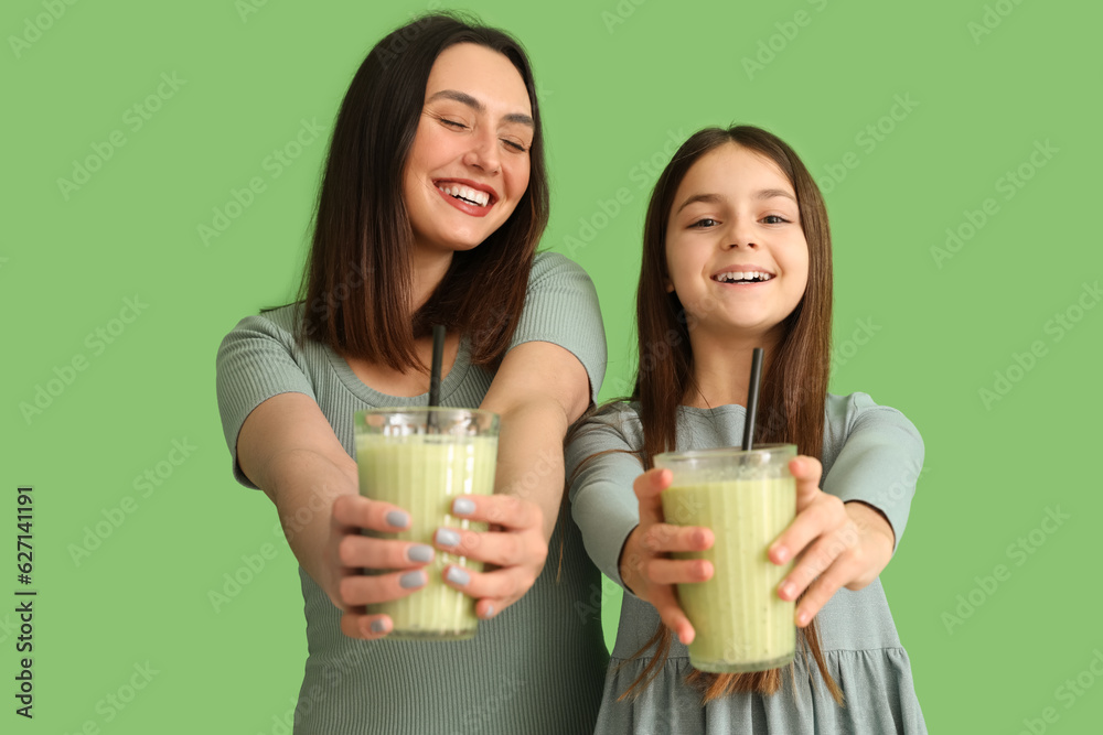 Little girl with her mother drinking smoothie on green background