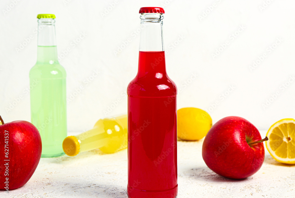 Bottles of fresh soda and fruits on light background, closeup