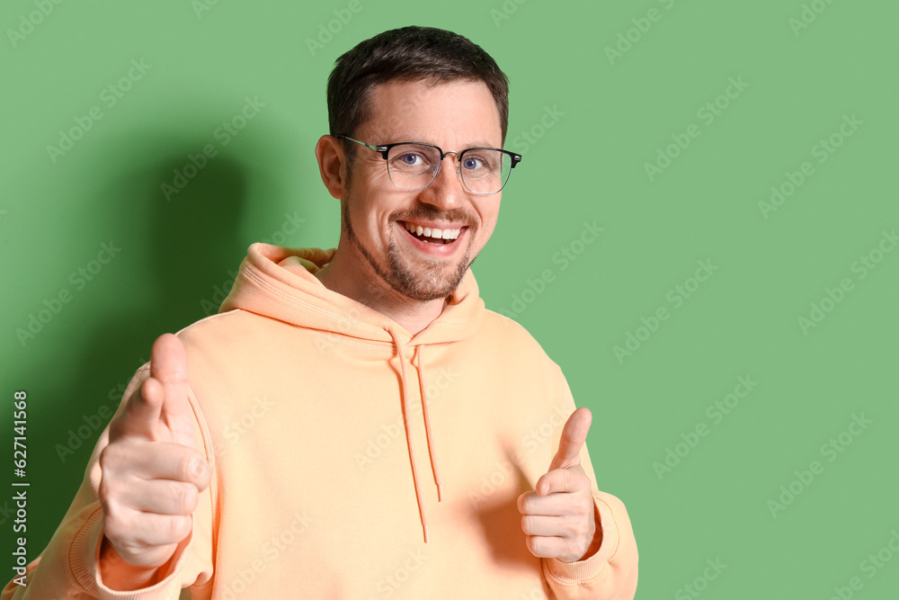 Handsome man in stylish eyeglasses pointing at viewer on green background, closeup