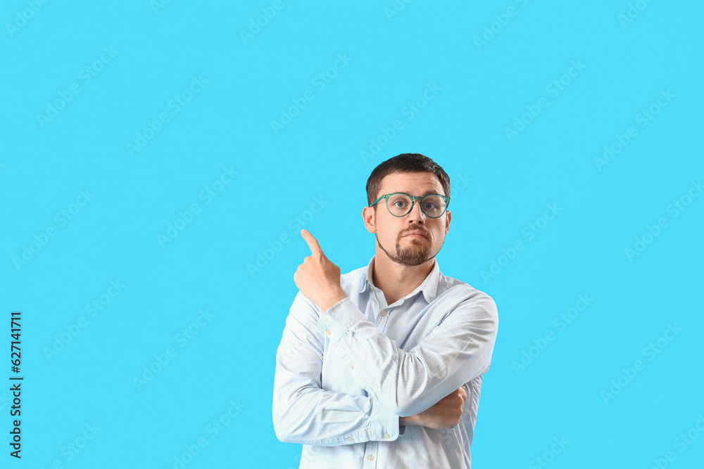 Handsome man in stylish eyeglasses pointing at something on blue background