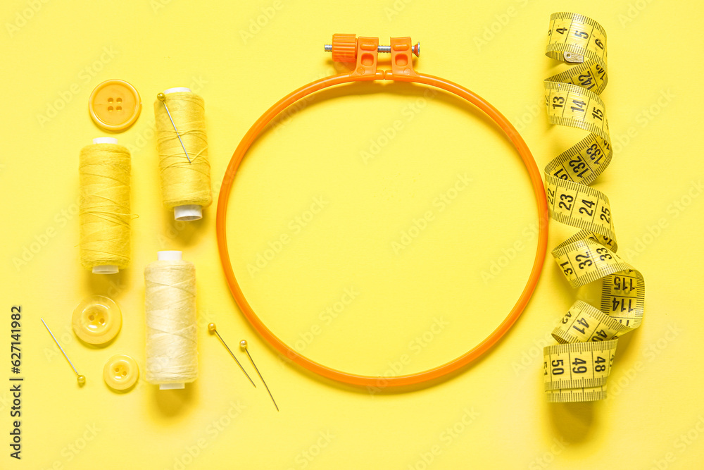 Embroidery hoop with thread spools and measuring tape on yellow background