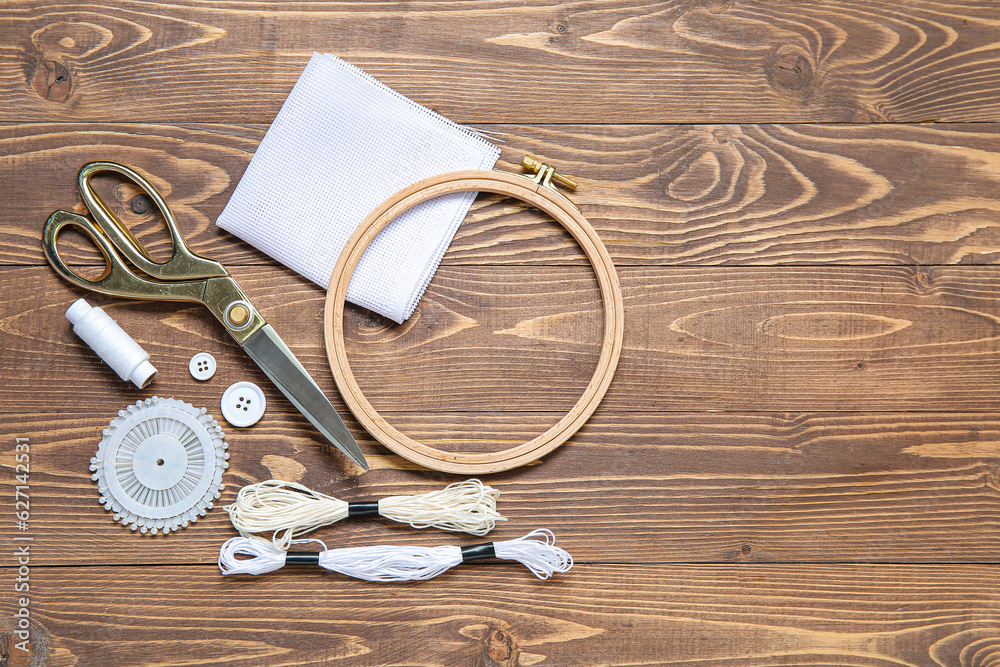 Embroidery hoop with canvas, scissors and mouline threads on brown wooden background