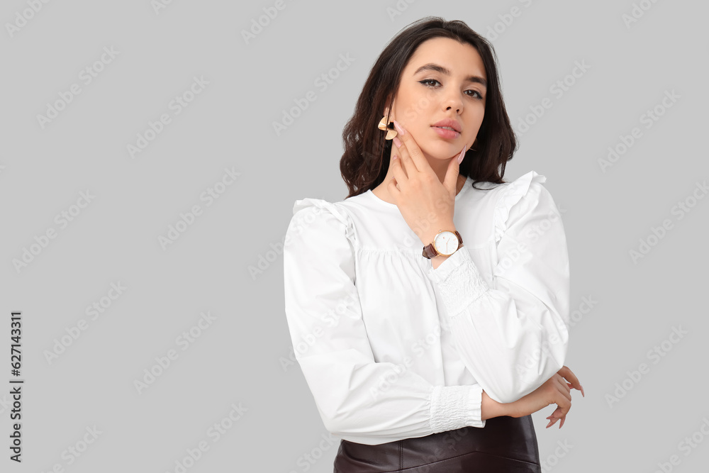 Beautiful young woman with wristwatch on grey background