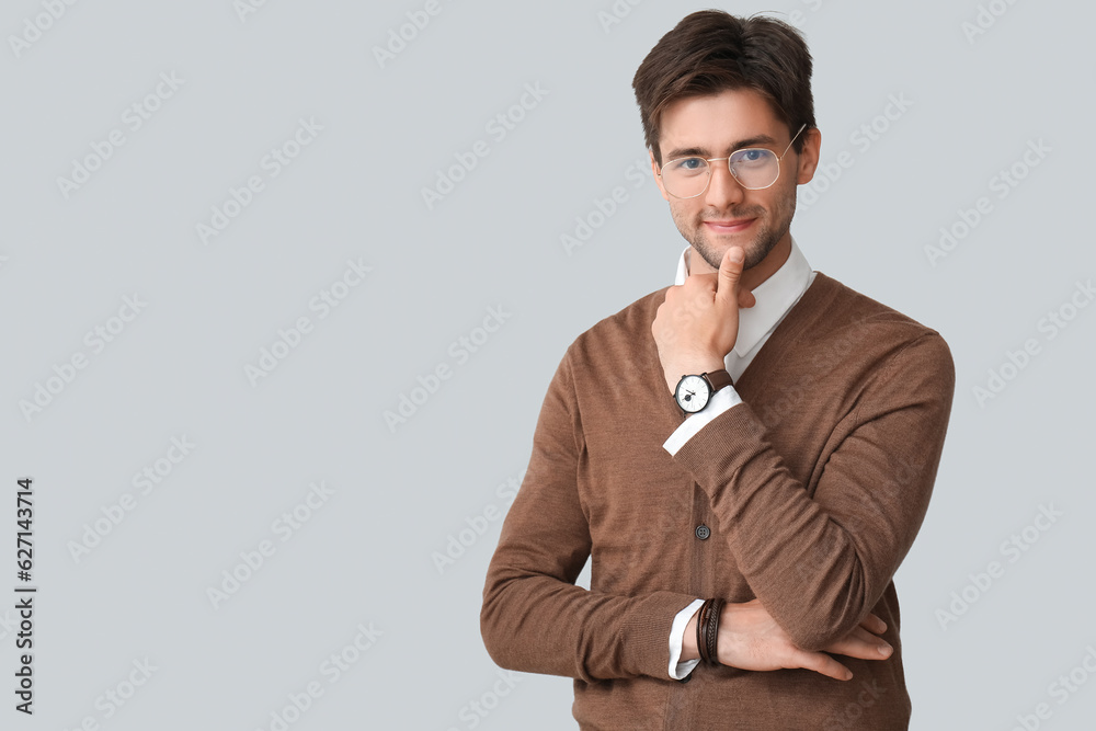 Stylish young handsome man in eyeglasses with wristwatch on grey background