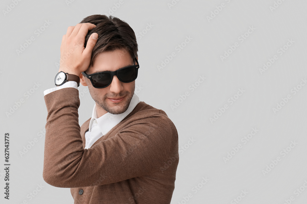 Handsome stylish young man in sunglasses with wristwatch on grey background