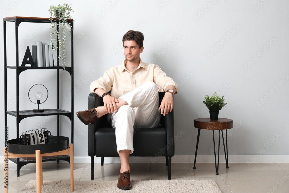 Handsome stylish young man with wristwatch sitting on armchair in room