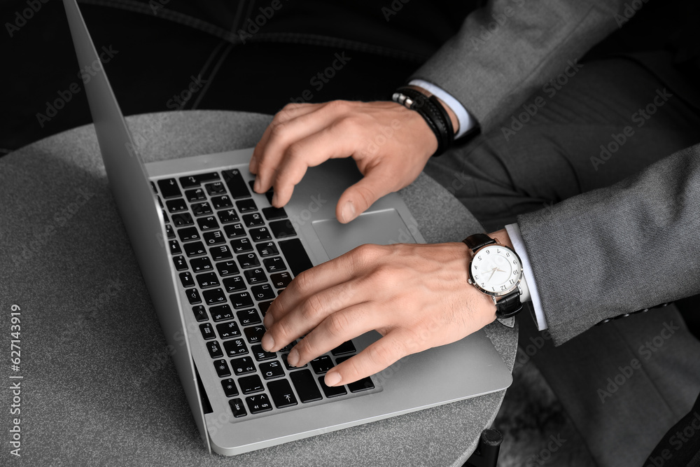 Young businessman in wristwatch working with laptop at table, closeup