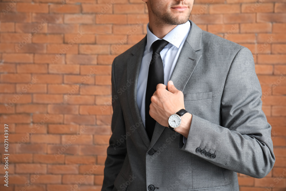 Stylish young man in suit with wristwatch against brick wall, closeup