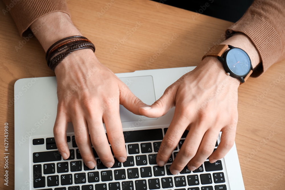 Stylish young man with wristwatch working on laptop at table in office, closeup