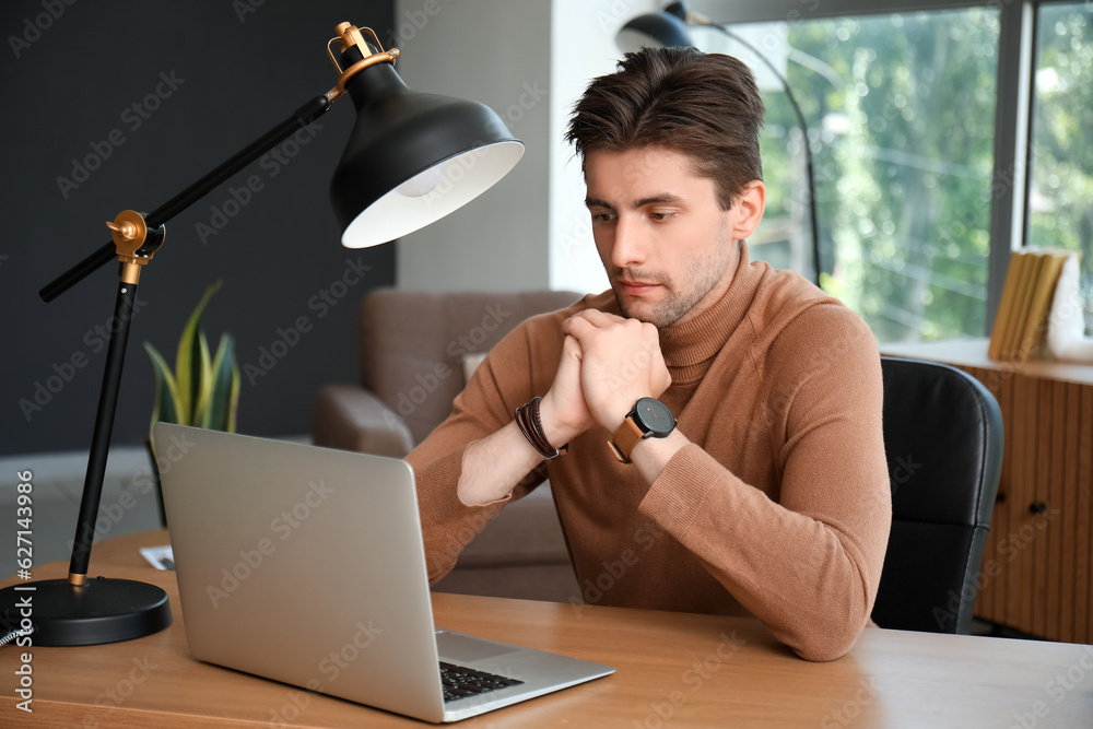 Stylish young man with wristwatch working on laptop at table in office, closeup