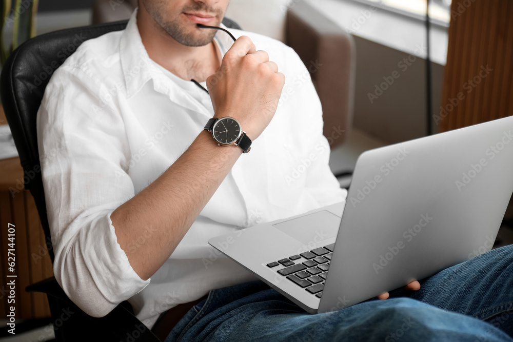 Handsome young man with wristwatch and eyeglasses working on laptop in office