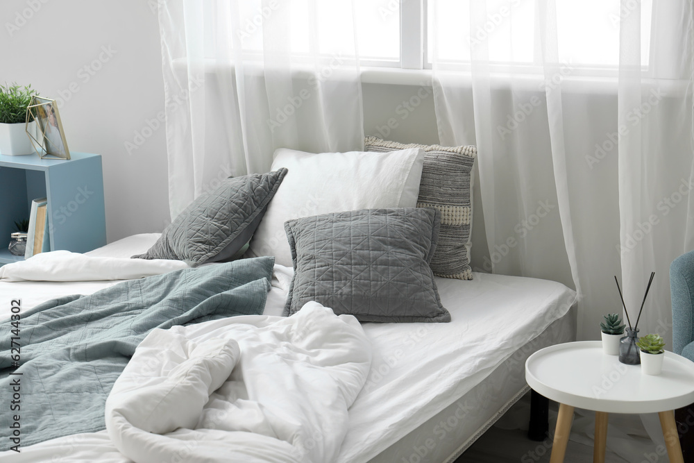 Cozy bed with soft pillows and crumpled blankets in childrens bedroom