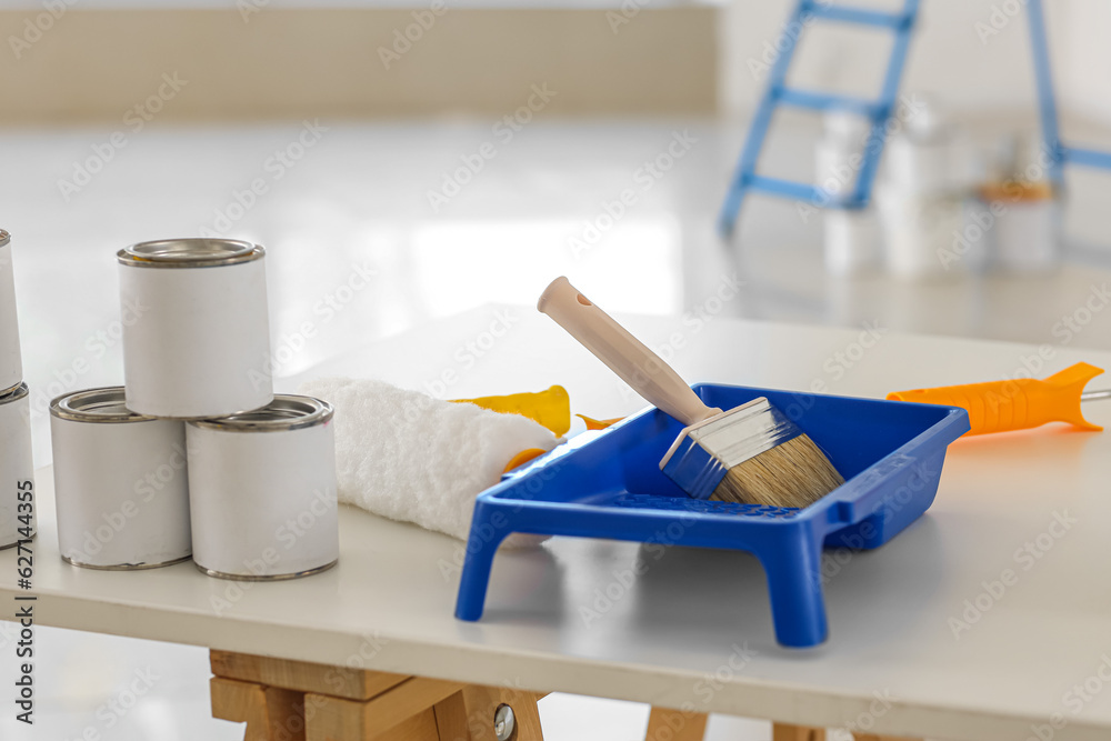 Paint brush with cans on table in room, closeup