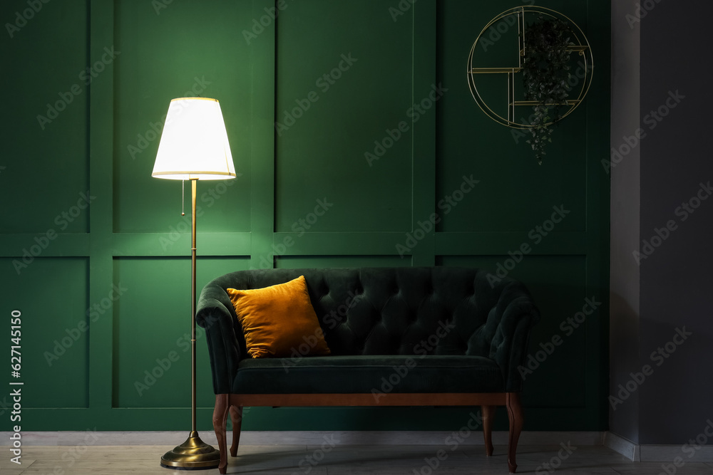 Glowing stand lamp with sofa near green wall in dark room