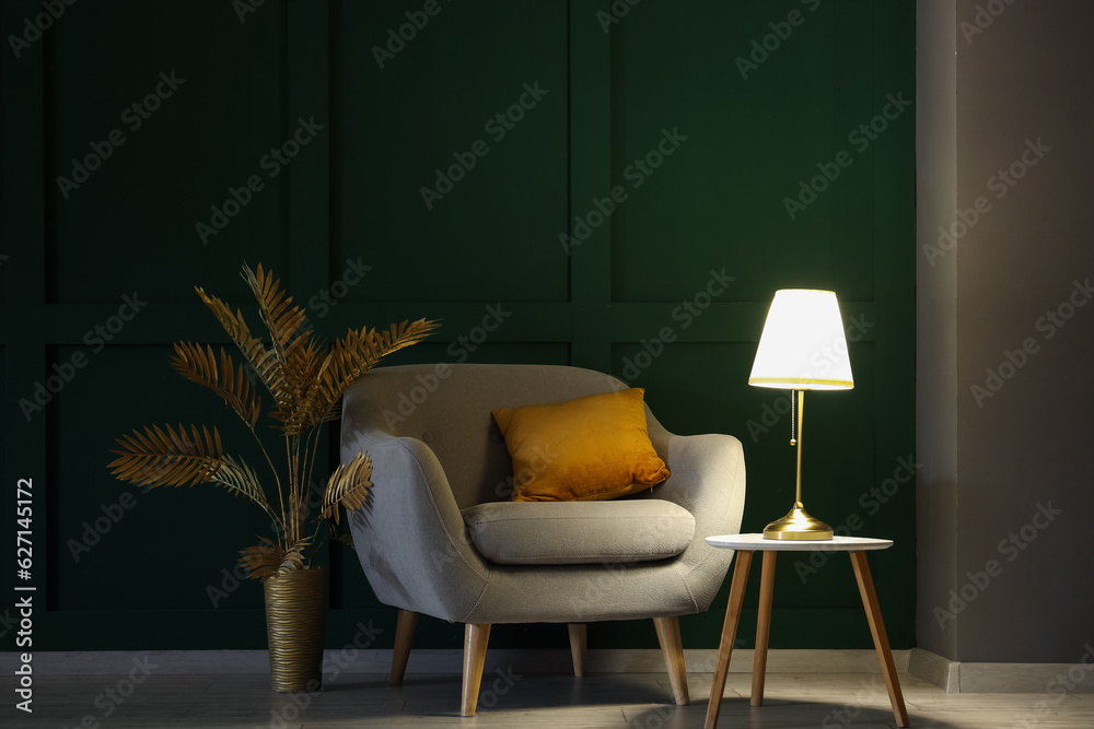 Interior of dark living room with glowing lamp on table and armchair