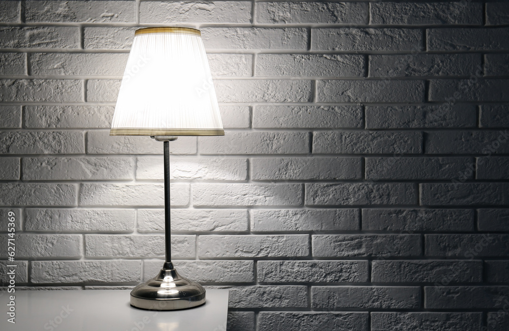 Glowing lamp on table near white brick wall in dark room