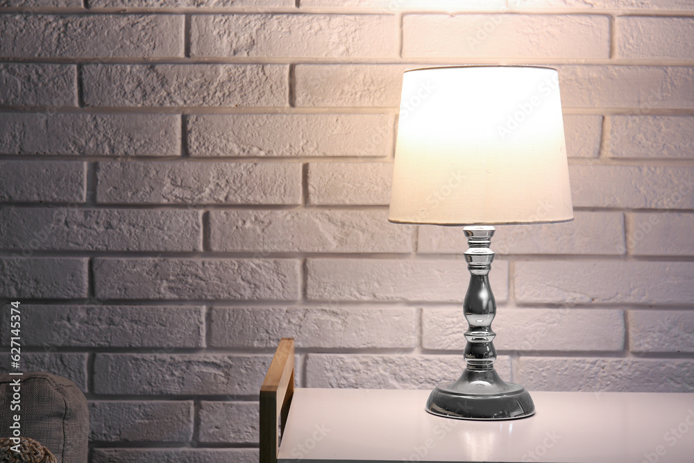 Glowing lamp on shelving unit near white brick wall in dark room