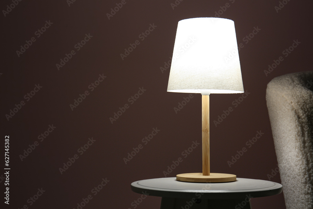 Glowing lamp on wooden table near sofa in dark room