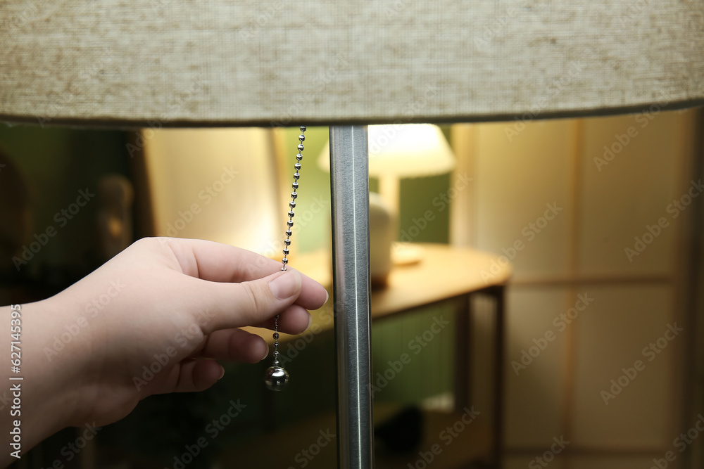 Woman turning on floor lamp in dark living room, closeup