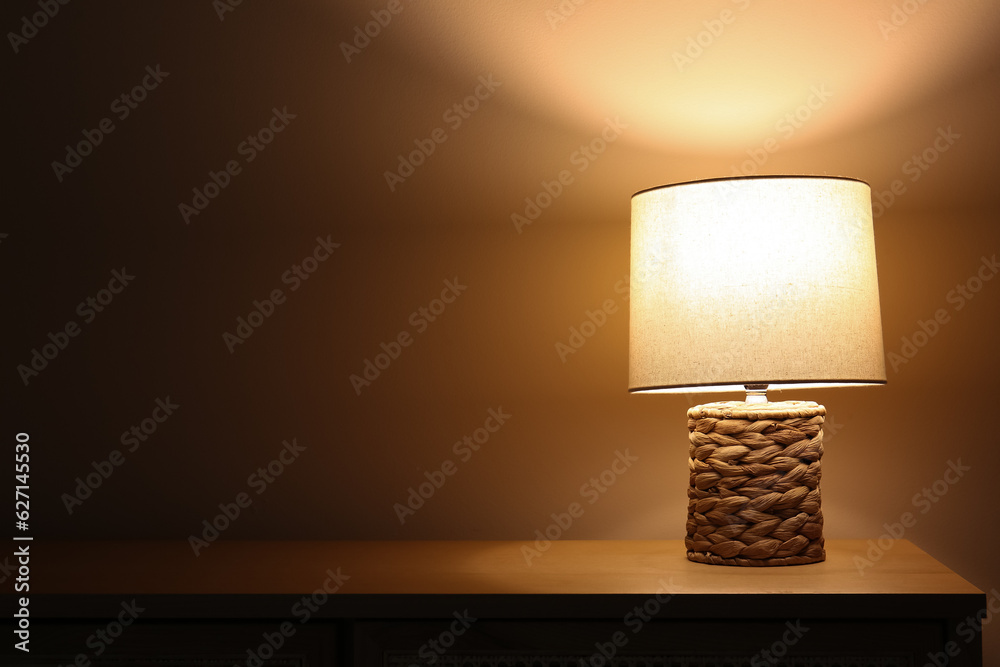 Glowing lamp on wooden table in dark room