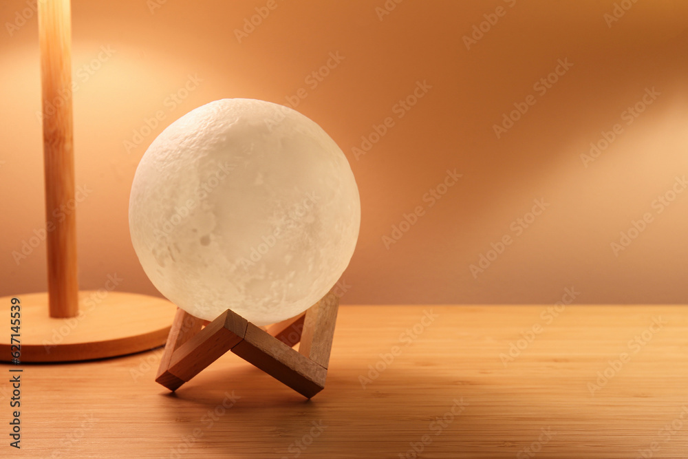 Glowing lamp in shape of moon on wooden table in dark room, closeup