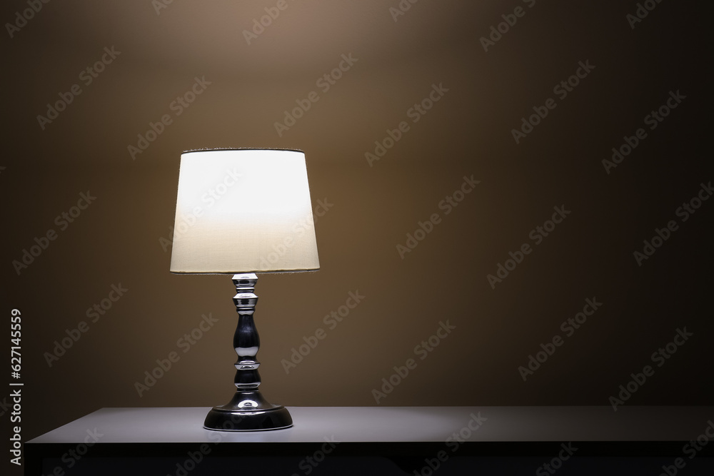 Glowing lamp on white table in dark room