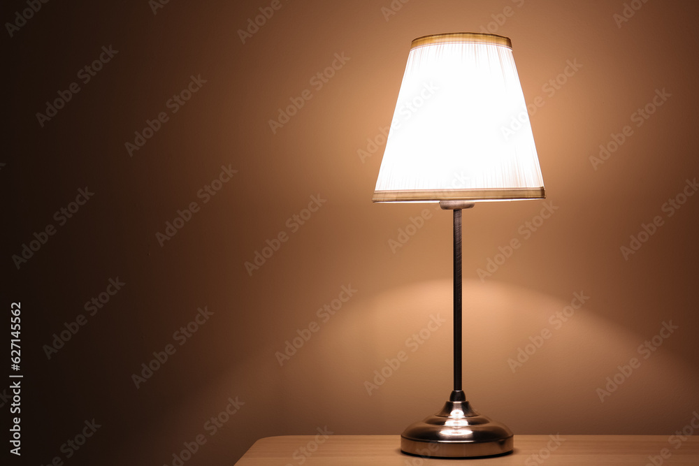 Glowing lamp on wooden table in dark room