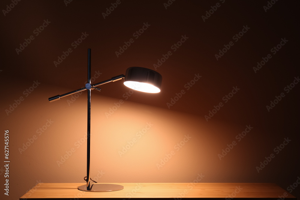 Glowing lamp on wooden table in dark room