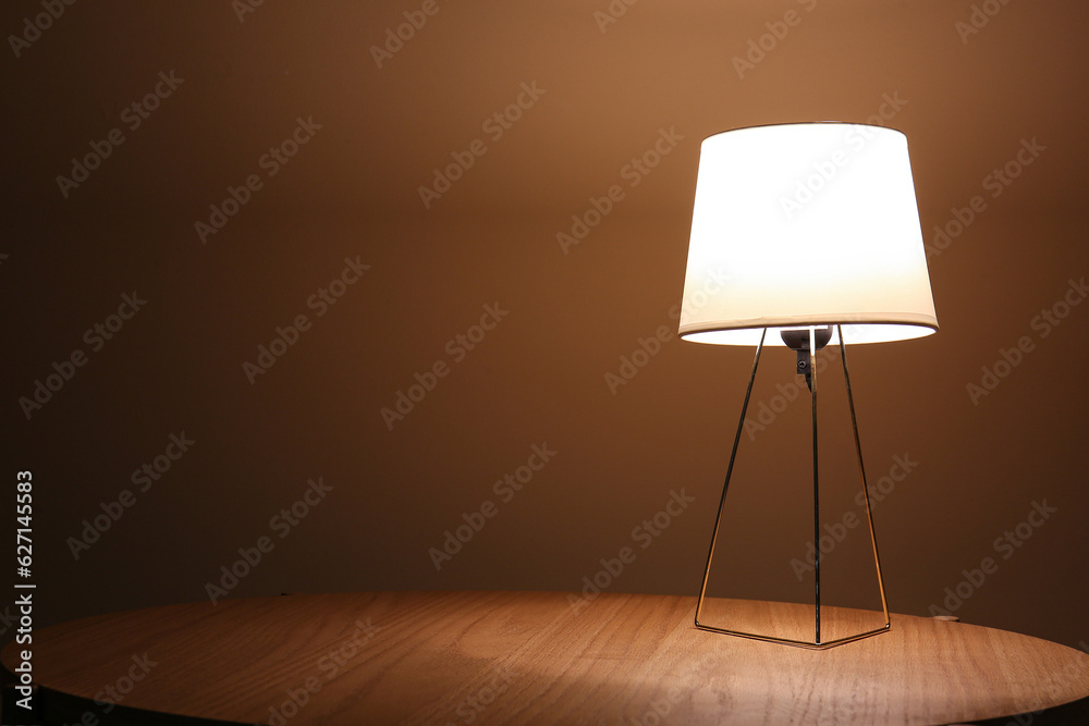 Glowing lamp on wooden table in dark room