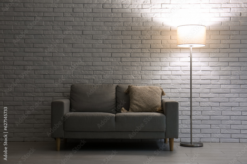 Glowing floor lamp near grey sofa in dark room