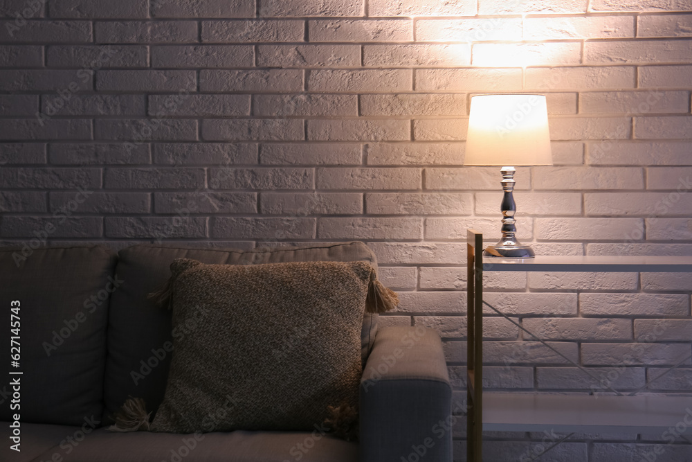 Glowing lamp on shelving unit near grey sofa in dark room