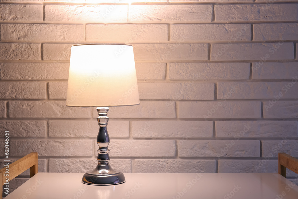 Glowing lamp on shelving unit near white brick wall in dark room