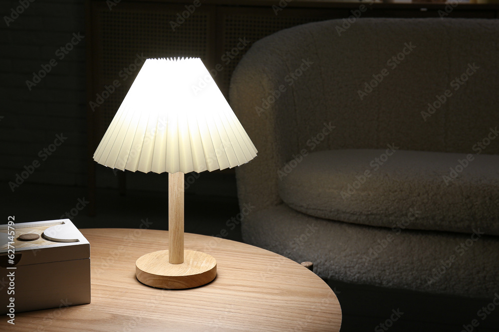 Glowing lamp on wooden table near white brick wall in dark room