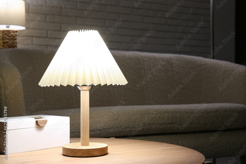 Glowing lamp on wooden table near white brick wall in dark room