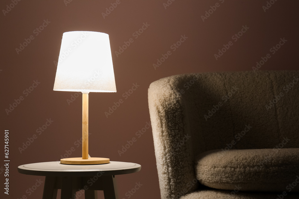 Glowing lamp on wooden table near sofa in dark room