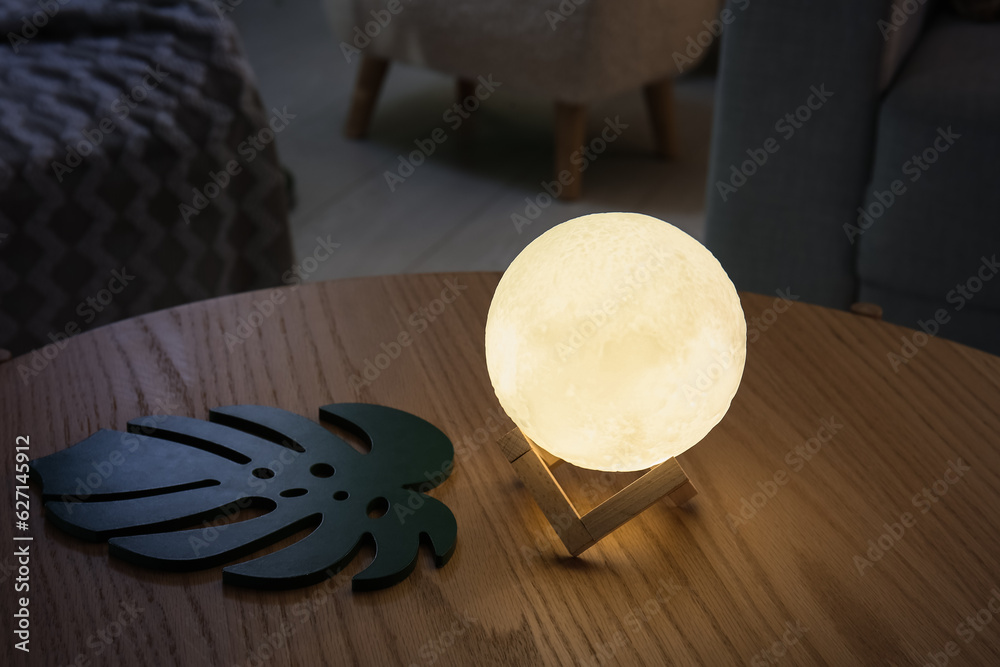 Glowing lamp in shape of moon on wooden table in living room, closeup