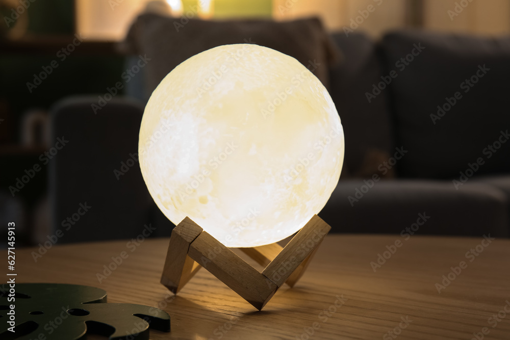 Glowing lamp in shape of moon on wooden table in living room, closeup