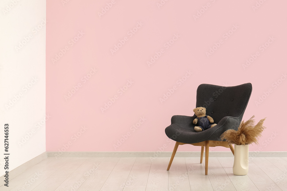 Grey armchair with teddy bear and pampas grass in vase near pink wall