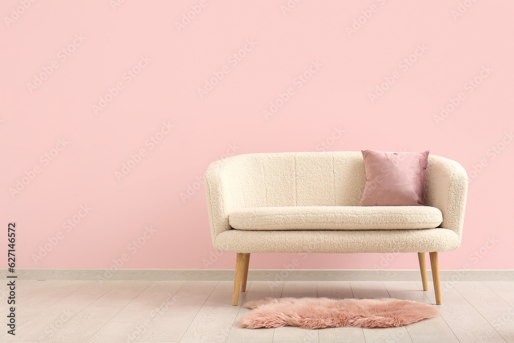 Cozy sofa with cushion and fur rug near pink wall