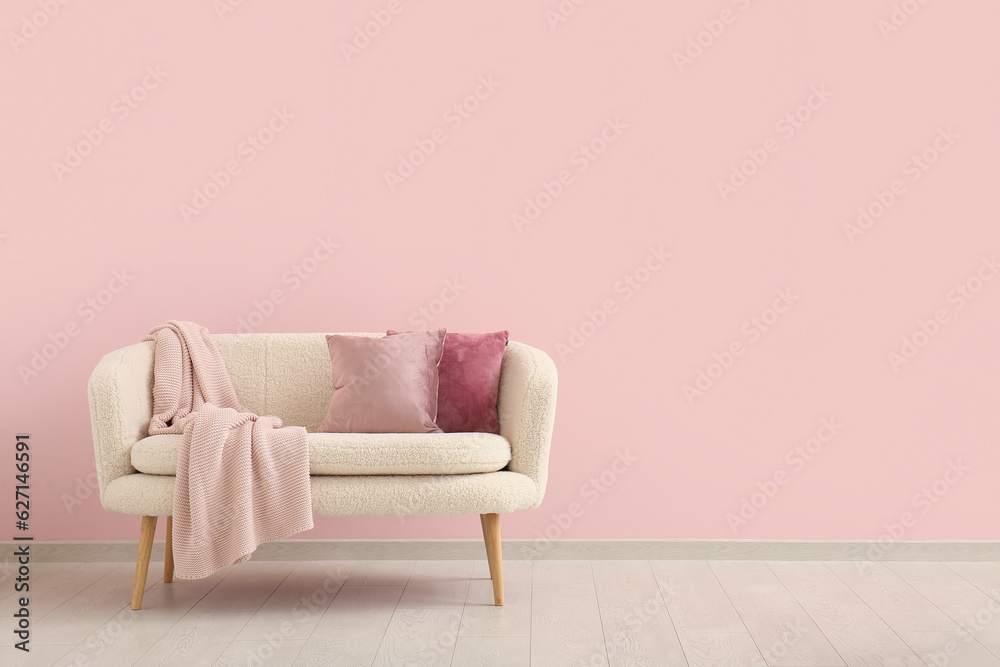 Cozy sofa with cushions and blanket near pink wall