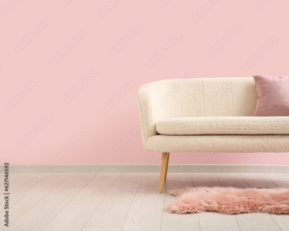 Cozy sofa with cushion and fur rug near pink wall