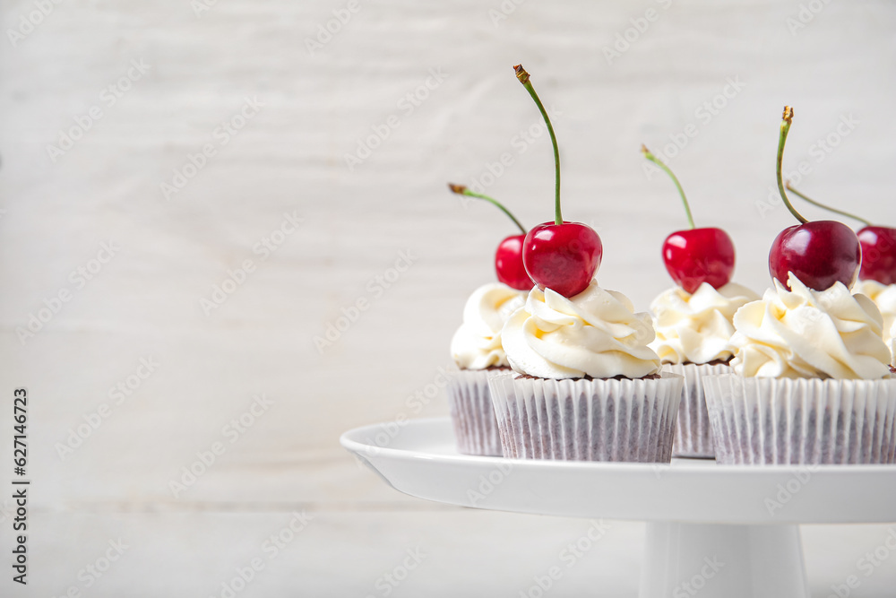 Stand with tasty cherry cupcakes on light background