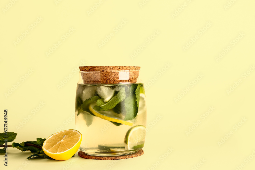 Glass jar of cold mojito, lemon and mint on color background